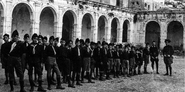 Jovens militantes do fascismo uniformizados e reunidos em frente aos portões de um edifício.