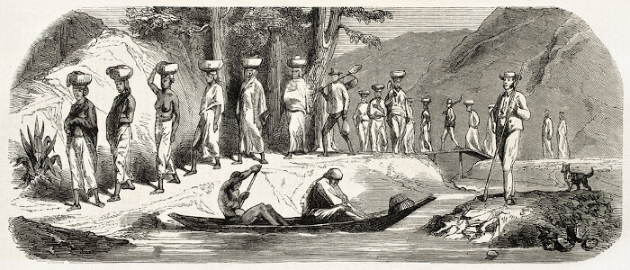 Trabalhadores à beira de um rio carregando trouxas na cabeça; a exploração é uma prática do imperialismo.