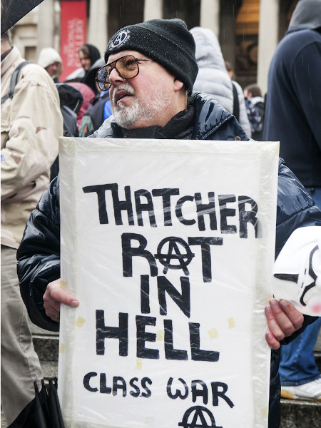 Manifestantes na PraÃ§a Trafalgar para comemorar a morte de Margaret Thatcher. Homem segura cartaz: â€œThatcher apodrece no infernoâ€.[1]