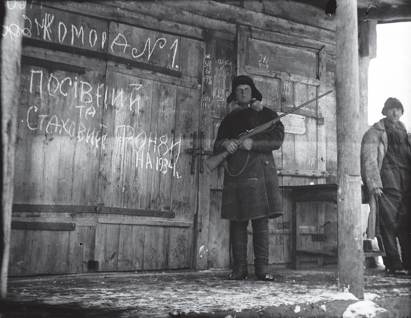 Guarda soviÃ©tico armado em frente a estoque de cereais na UcrÃ¢nia.