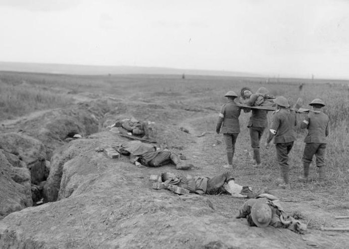 Soldados carregam ferido enquanto passam por corpos no chÃ£o em trincheira durante a Primeira Guerra Mundial.