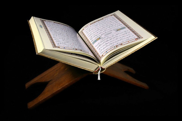 Exemplar do Alcorão, livro sagrado do islamismo, aberto sobre um suporte de madeira.