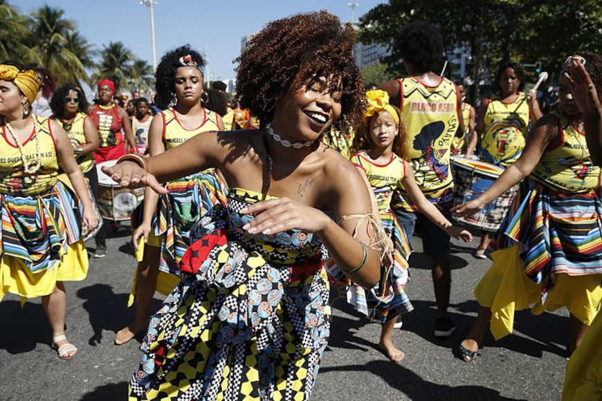 Mulher com trajes tÃ­picos, danÃ§ando, em texto movimento negro.